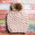 A generous faux fur pom-pom looks like real fur, on a colorful chunky knit hat.
